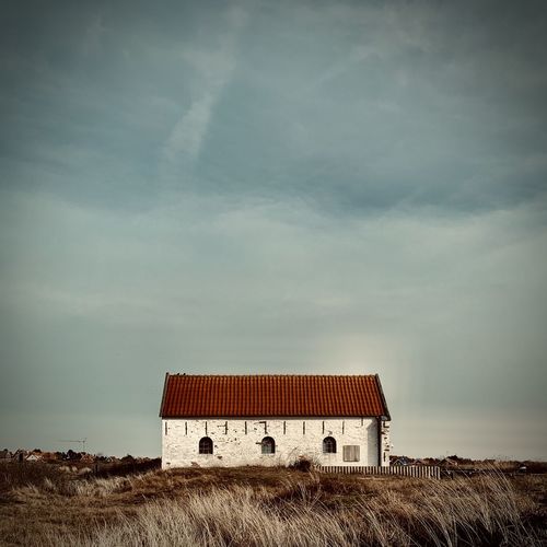 Barn on field by building against sky
