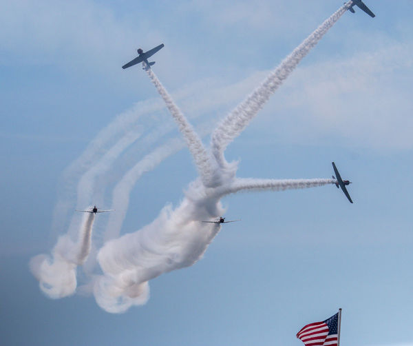 The skytypers  airplane team leaving a smoke design in the sky over an american flag.