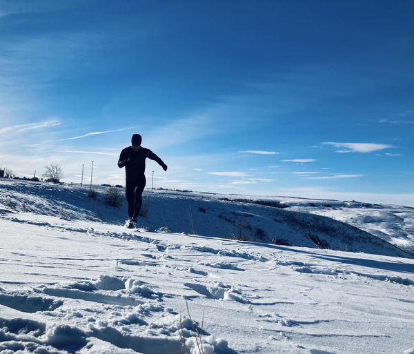 Full length of man running in snow covered land against sky