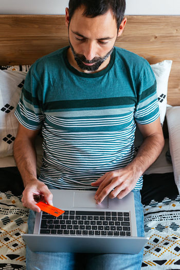 Man shopping online on a laptop lying on the bed at home