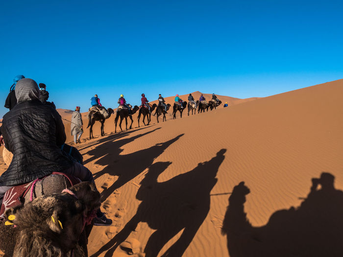 GROUP OF PEOPLE RIDING IN DESERT AGAINST SKY