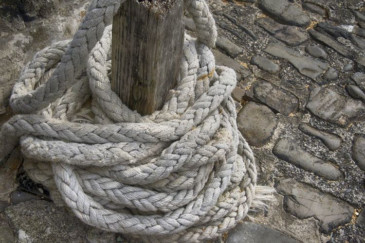 High angle view of rope tied to wooden post on cobbled pathway