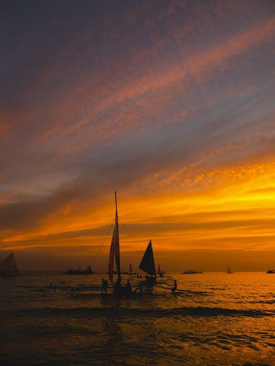 Silhouette sailboat in sea against sky during sunset