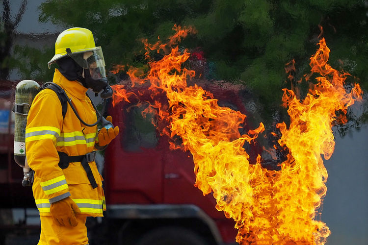 Side view of firefighter by fire against fire engine