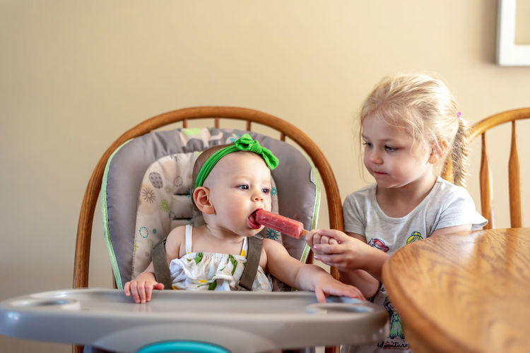 Girl feeding flavored ice to baby sister at home