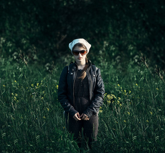 Portrait of young woman wearing sunglasses while standing on grassy field