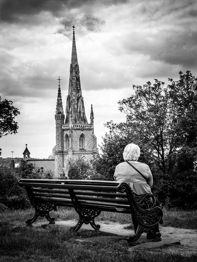 Rear view of senior woman sitting on bench against church