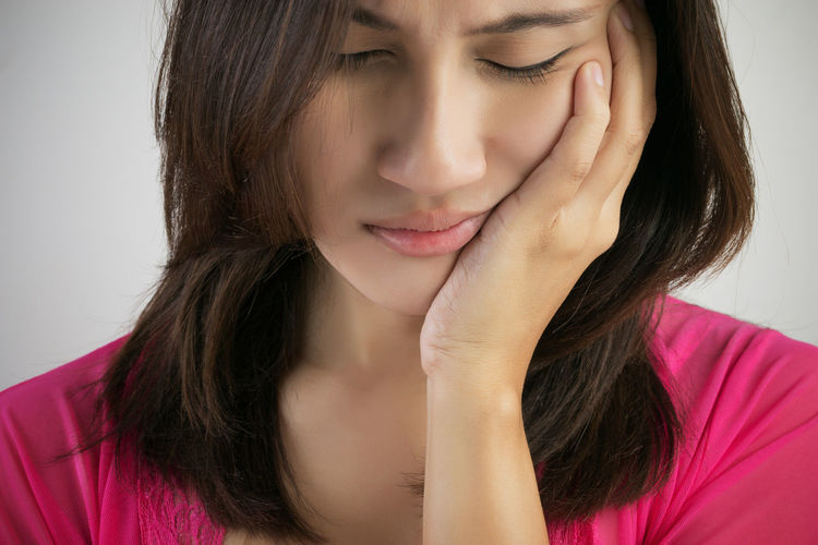 Young woman suffering from toothache against gray background