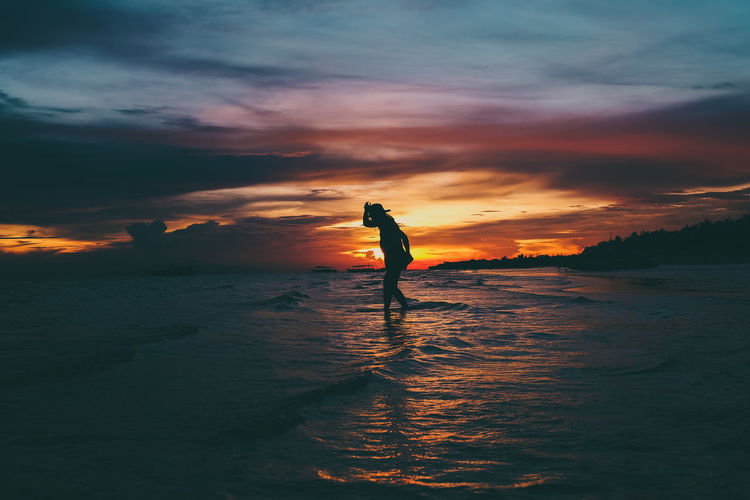 Silhouette woman wading in sea against sky during sunset