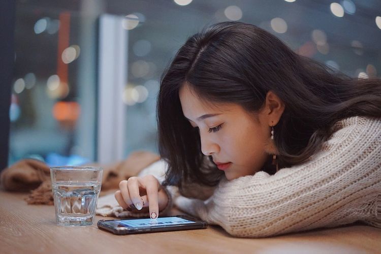 Close-up of young woman using mobile phone while leaning on table