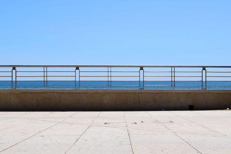 Empty pedestrian zone by sea against clear blue sky