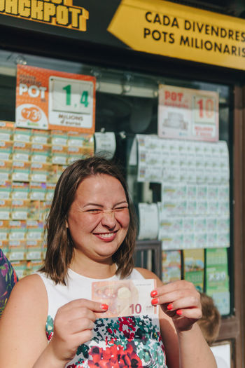 Smiling woman holding paper currency while standing against store