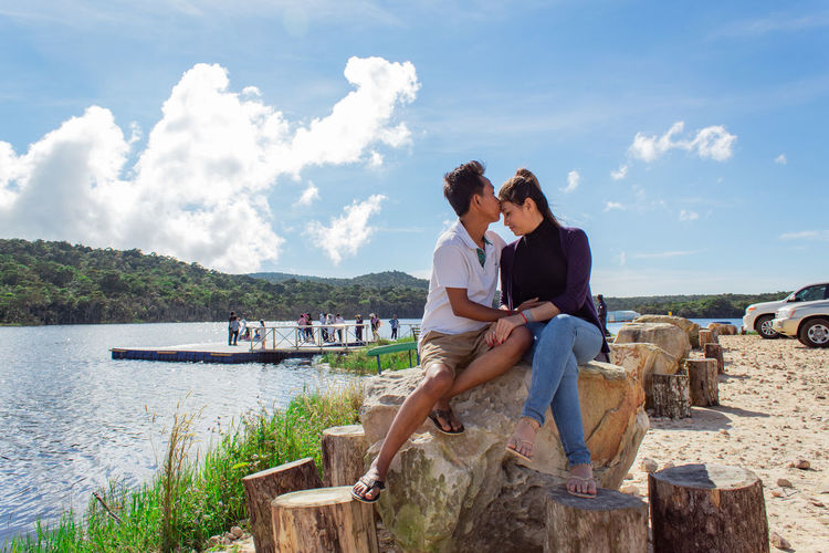 Young couple sitting on rock against sky