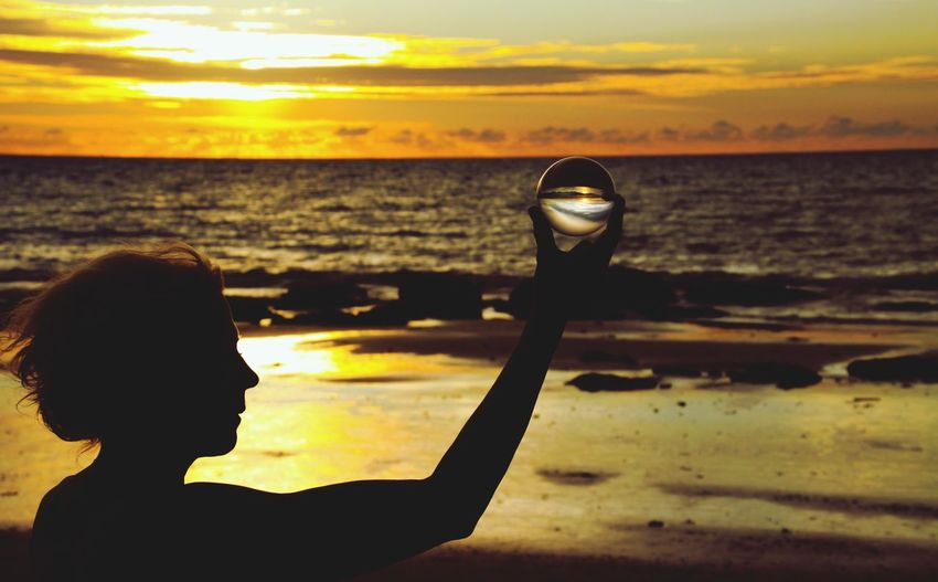 Silhouette woman holding crystal ball at beach against sky during sunset