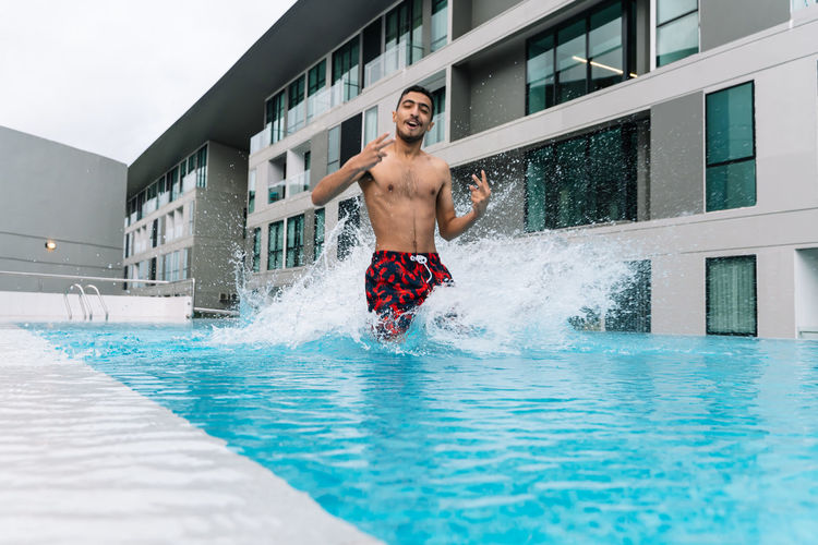 Young man jumping into a pool surrounded by buildings