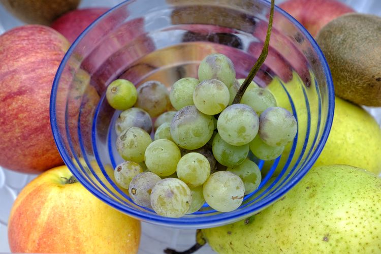 A blue glass bowl of very ripe grapes, on top of other variegated fruit 
