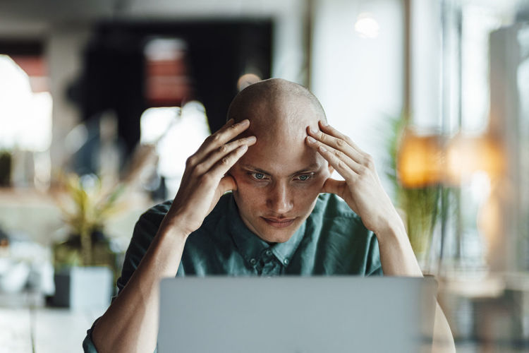 Worried young businessman with head in hands looking at laptop in cafe
