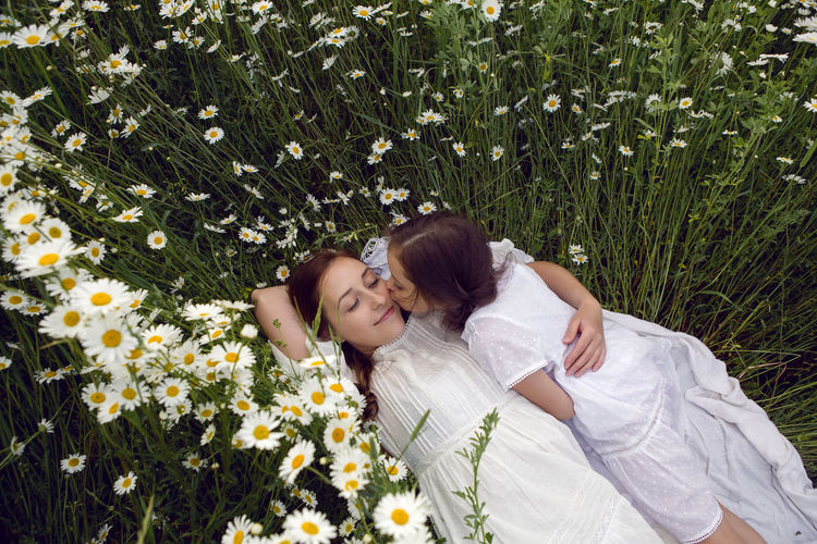 Mother with daughter in a white dress lie on a camomile field