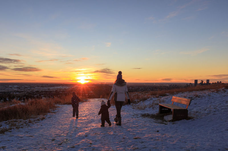 People on snow covered land against sky during sunset