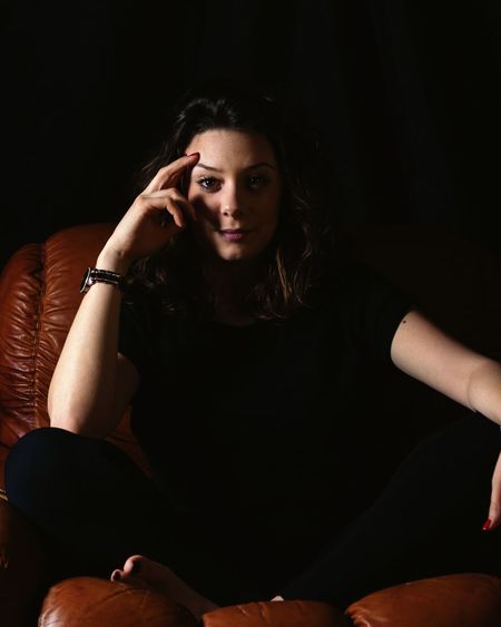 Portrait of a young woman sitting against black background