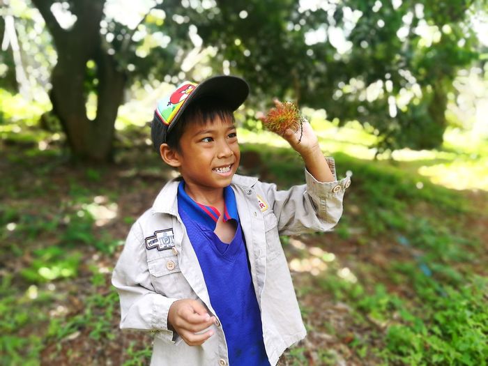 Smiling boy holding rambutan while standing on field