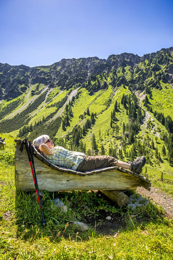 Senior woman lying on wooden bench, mountain nebelhorn, allgau, bavaria, germany