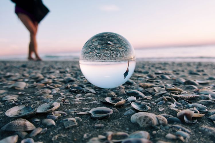 Crystal ball on beach reflecting woman walking 
