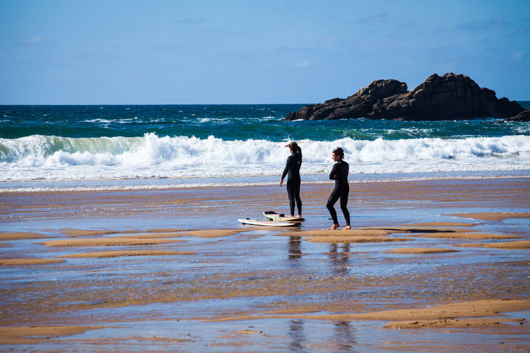 Full length of man and women with surfboard standing on beach against sky