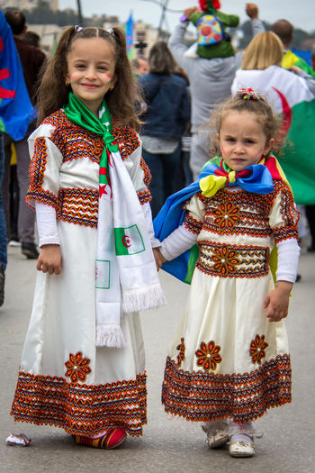 Siblings in traditional clothing standing outdoors during event 