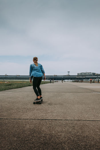 Rear view of woman standing on skateboard against sky