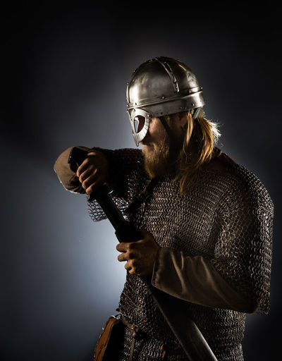 Viking wearing helmet and sword against black background