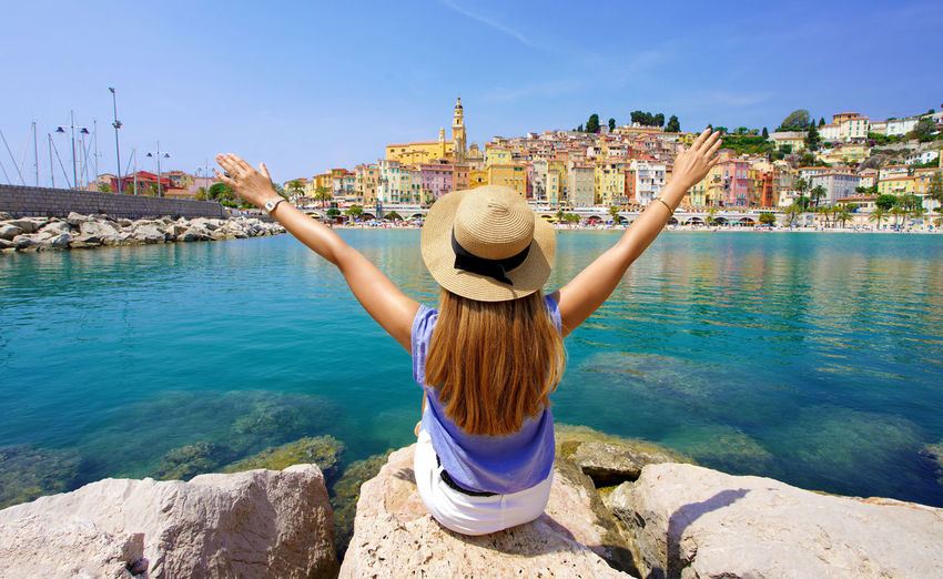 Panoramic view of traveler girl with arms raised enjoying view of menton village, french riviera.