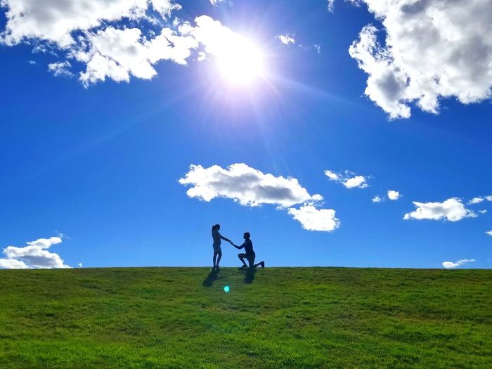 Man proposing woman on field against sky