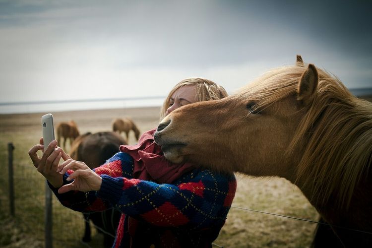 Young woman taking selfie with brown horse in ranch