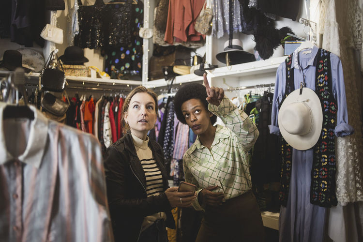 African female owner pointing while standing by customer in clothing store