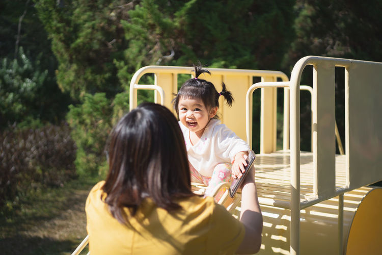 Rear view of mother playing with cheerful daughter at playground
