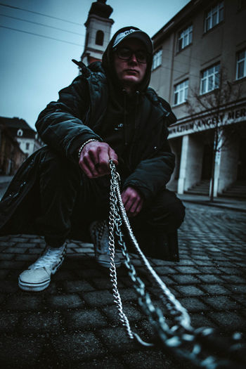 Full length of young man holding chain crouching on street