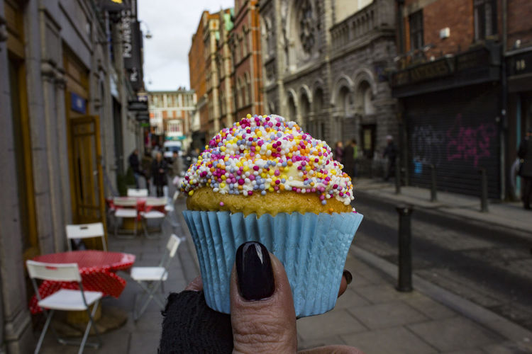 Close-up of hand holding cupcake against buildings