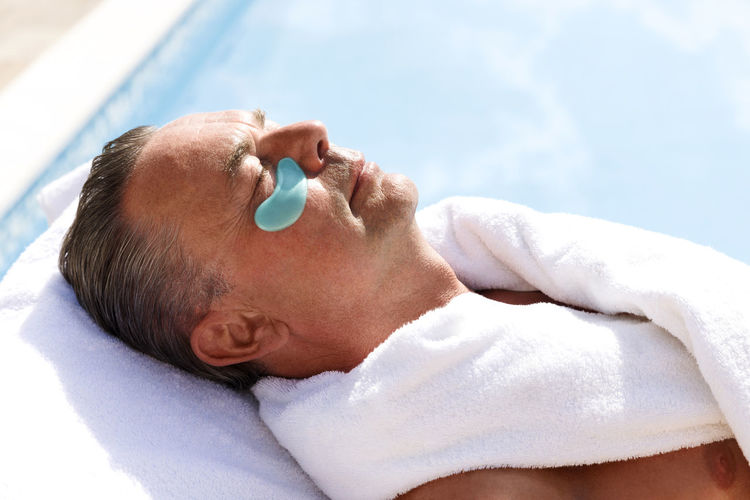 Mature man with collagen patch below eye at pool spa