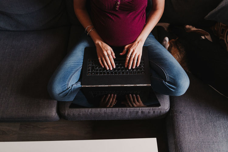 Midsection of pregnant woman using laptop while sitting on sofa at home