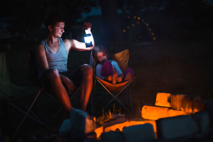 Father and daughter camping by bonfire at night