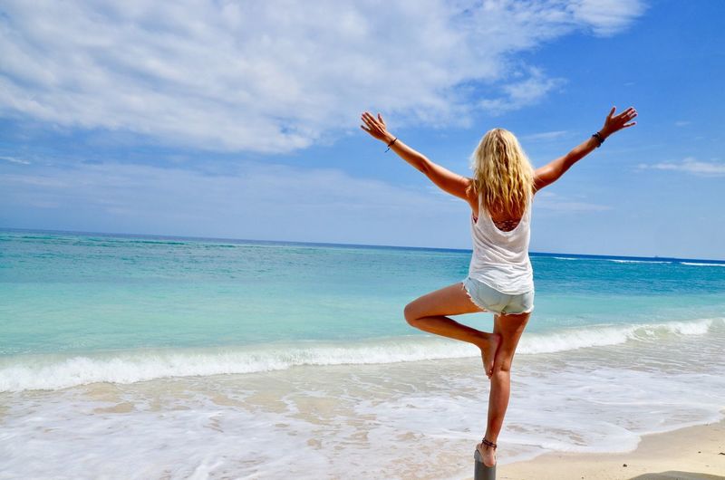 Rear view of woman standing with arms outstretched at beach against sky