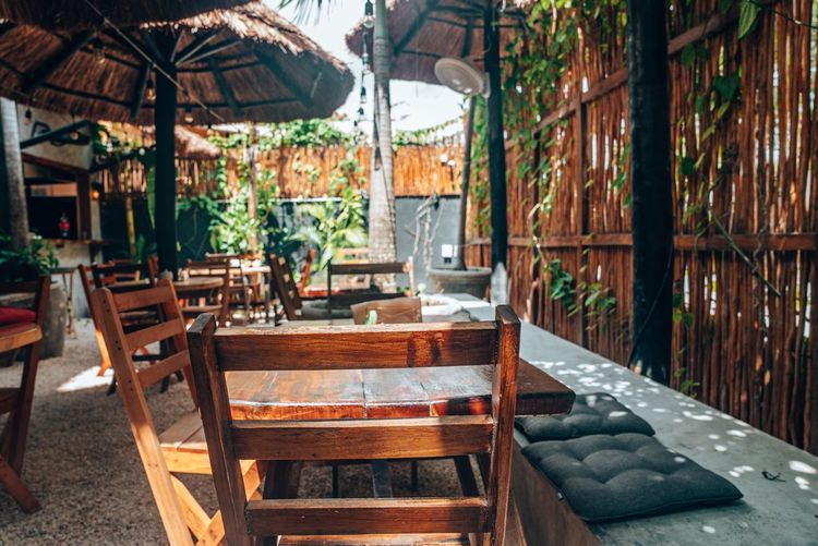 Empty wooden chairs and tables with straw umbrella at outdoor cafe