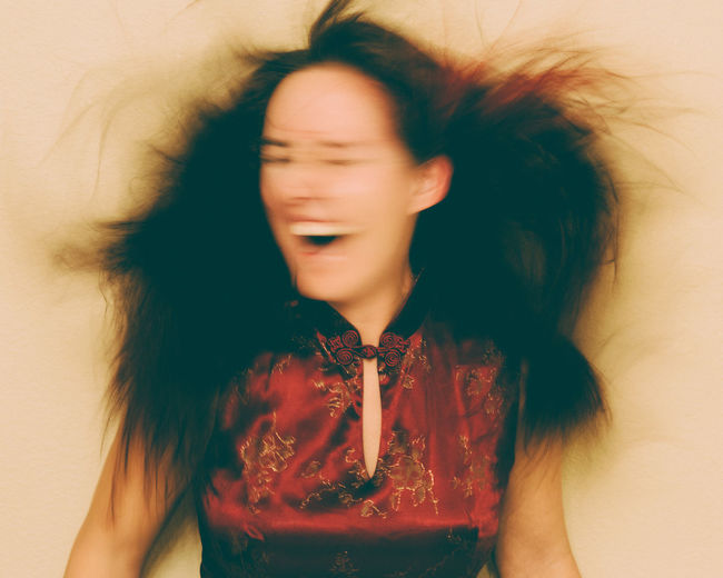 Blurred motion of smiling young woman against beige background