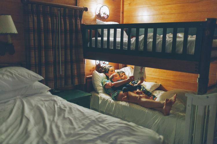 Mother with son reading book while lying on bed at home