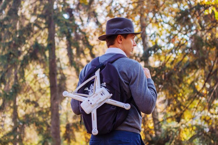 Man with drone standing against trees in forest