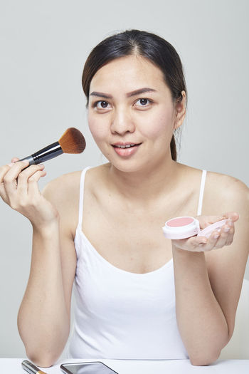 Portrait of beautiful mid adult woman applying make-up over gray background
