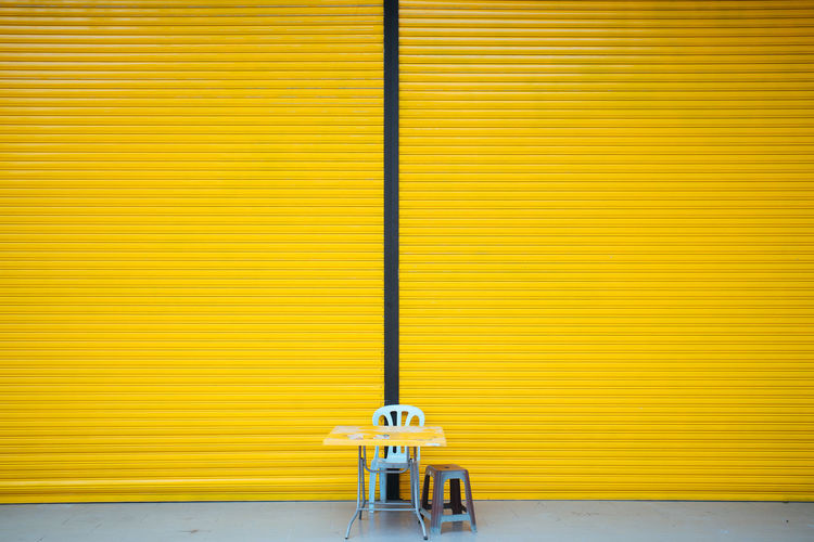 Chair and table against yellow closed shutter