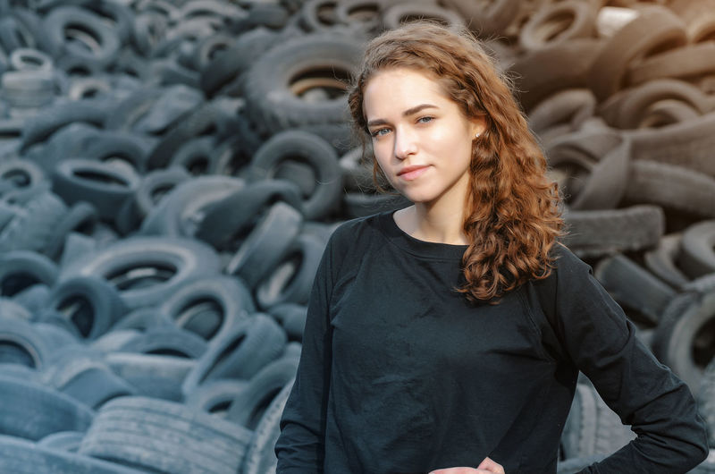 Portrait of young woman with long hair standing by tires