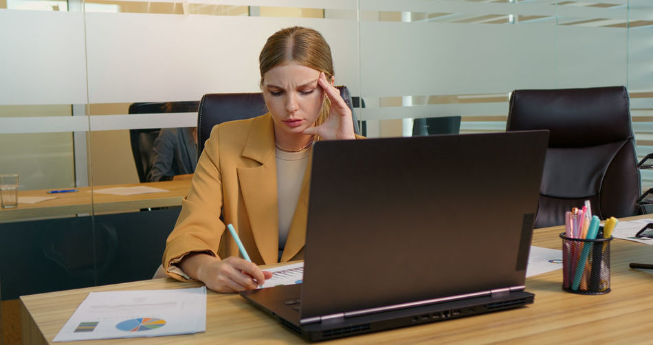 Businesswoman suffering from headache due to computer overwork. workaholic people concept.